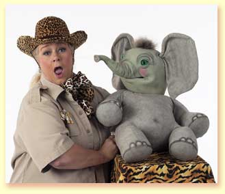 Photograph of Margaret Clauder as Masai Maggie, with the elephant puppet Sneezy, squirting her with water.