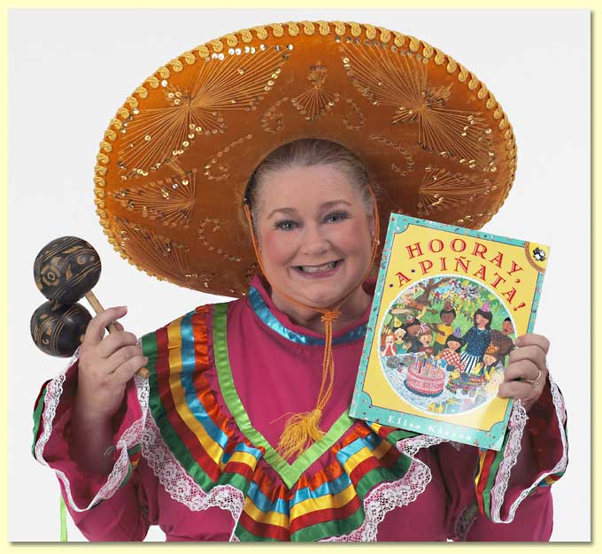Photograph of Margaret Clauder with musical shakers, in a Mexican dress with the book Hooray A Pinata.